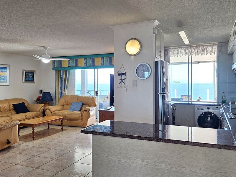 Open plan living and kitchen area featuring tiled floors, granite countertops, and direct access to a balcony with ocean views.