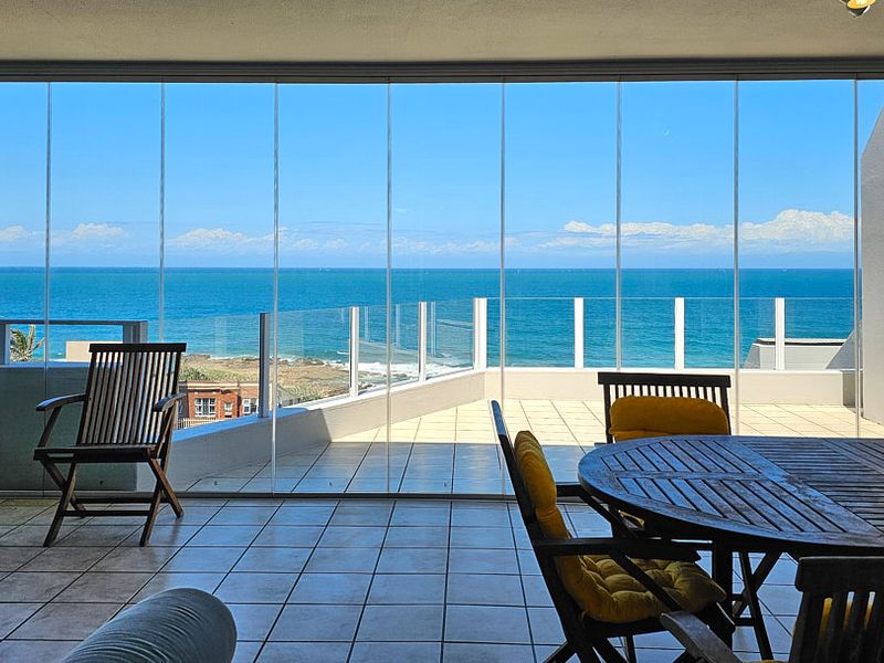 Spacious covered balcony featuring a glass enclosure, tiled flooring, and a glass balustrade, offering expansive ocean views.