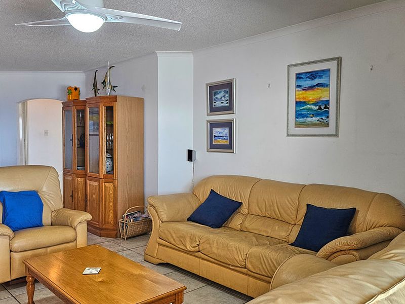 A comfortable living room featuring tiled flooring, a ceiling fan, and an open archway leading to adjacent areas.
