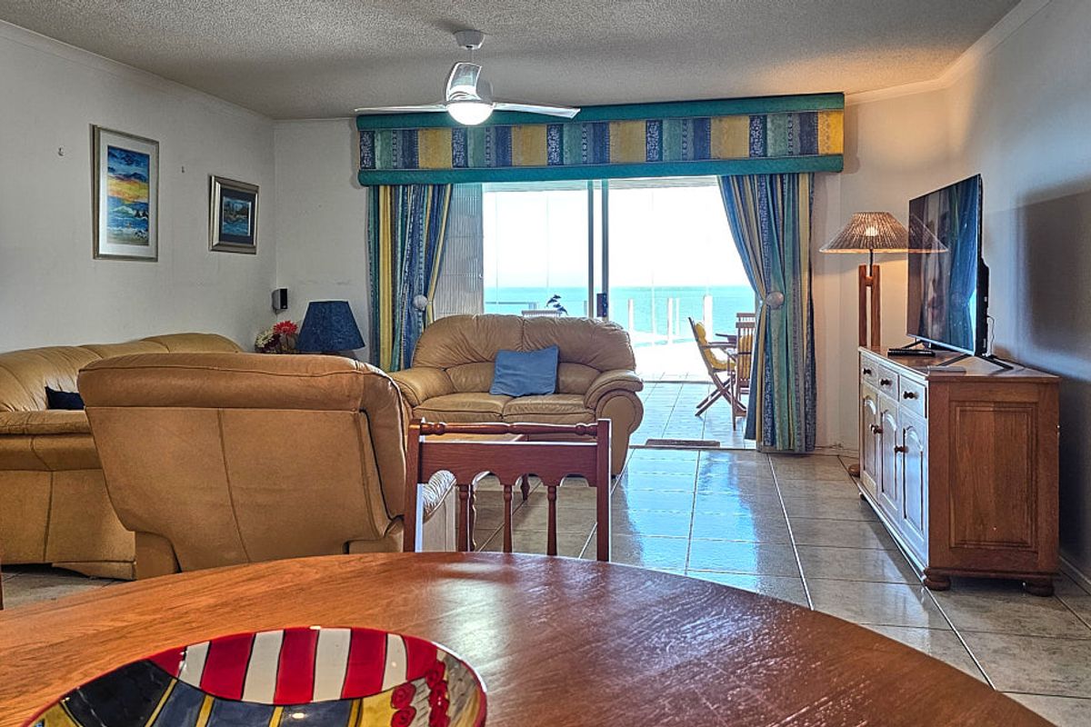 Spacious living area featuring tiled flooring, a ceiling fan, and large sliding glass doors providing direct access to a balcony with ocean views.