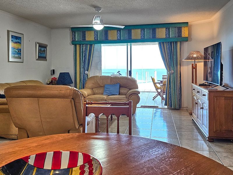 Spacious living area featuring tiled flooring, a ceiling fan, and large sliding glass doors providing direct access to a balcony with ocean views.