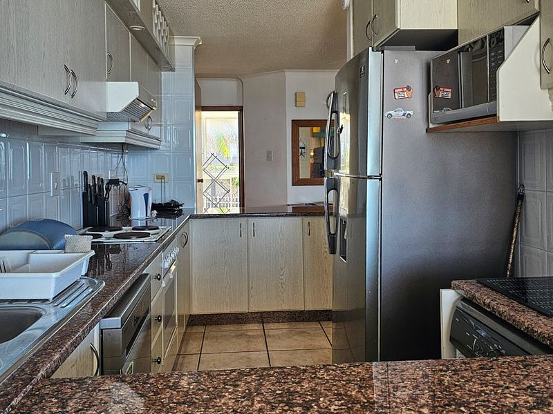 A functional galley-style kitchen featuring granite countertops, tiled backsplash, and ample built-in cabinetry, offering a practical layout for daily meal preparation.
