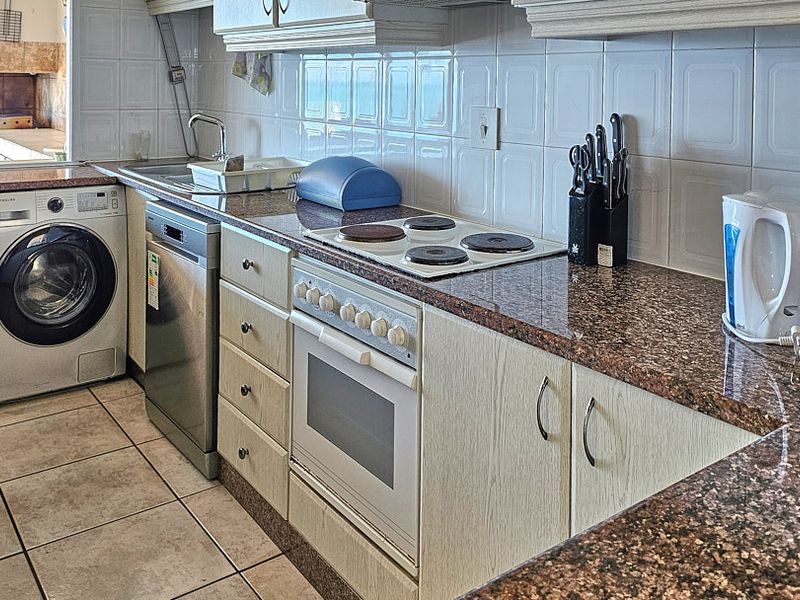 A functional kitchen featuring granite countertops, built-in oven, electric hob, and tiled backsplash with integrated space for laundry appliances.