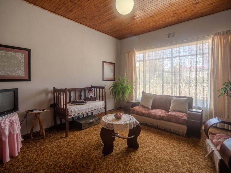 A living room featuring a timber tongue and groove ceiling, large window with security bars, and carpet flooring.