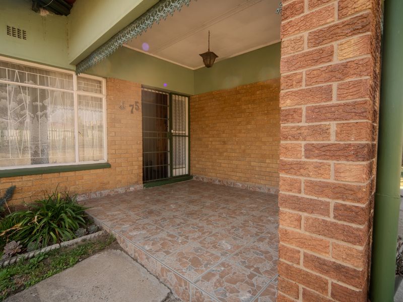 A covered front porch featuring face-brick walls, tiled flooring, and a security gate entrance, providing a classic and secure entry point to the home.