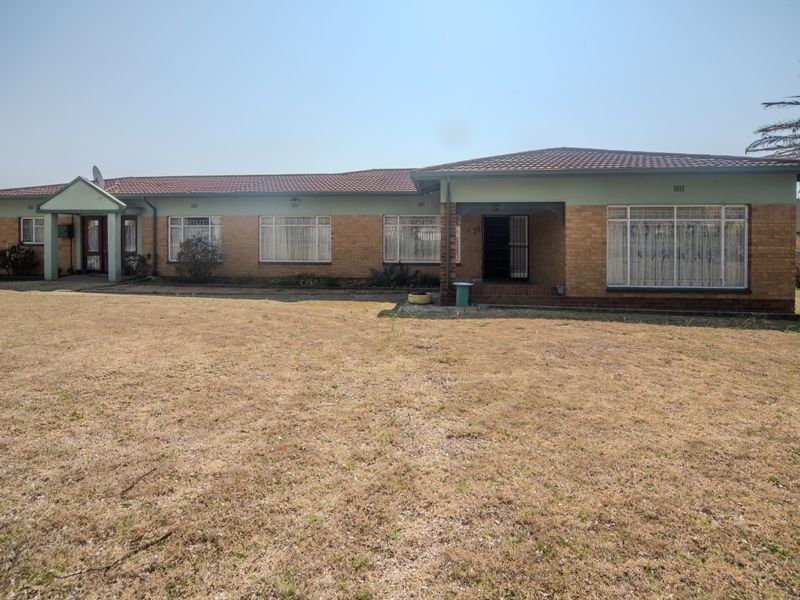 A single-story brick house with a tiled roof, featuring a large front lawn and covered entrance area.