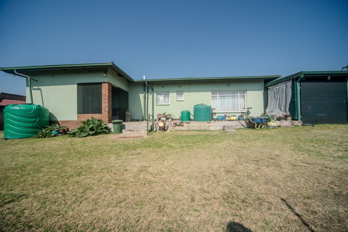 Rear view of the house featuring a concrete patio, green exterior walls, and a large backyard with water storage tanks.