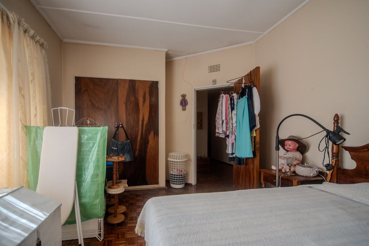 A bedroom featuring parquet flooring and a built-in wooden wardrobe, showing signs of wear and a visible wall crack above the doorway.