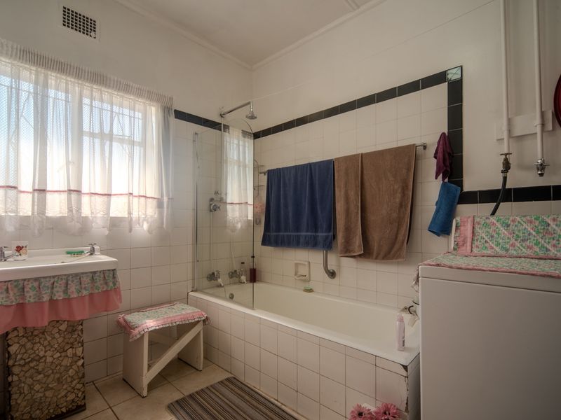 A dated bathroom featuring a bathtub with a glass screen, wall-mounted basin, and classic tiled finishes, offering potential for a modern renovation.