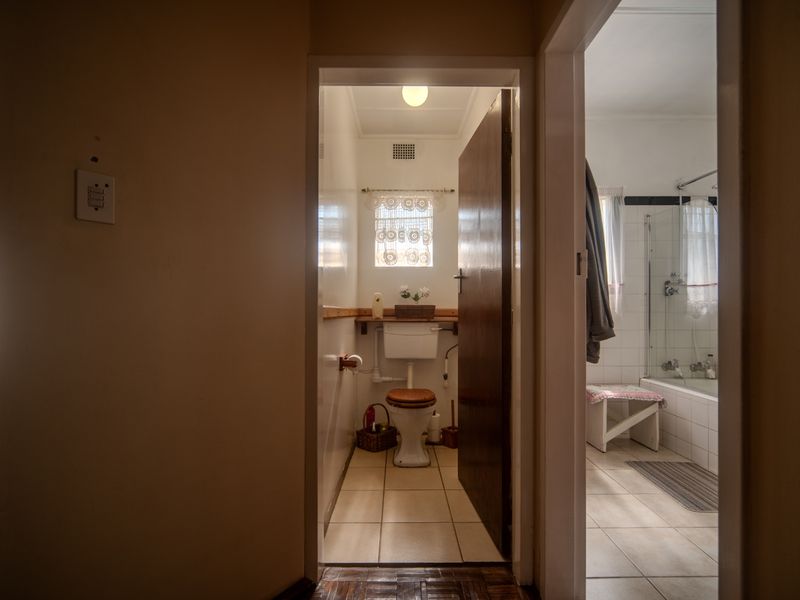 A view from the hallway into a separate toilet and adjacent bathroom featuring a bathtub with shower screen and tiled finishes.