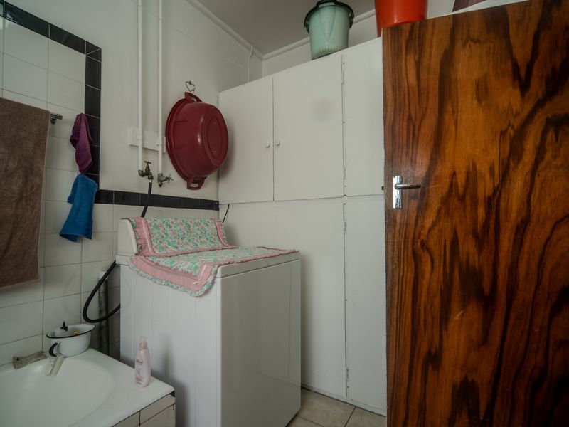 A functional laundry area featuring built-in storage cabinetry, tiled wall finishes, and dedicated plumbing connections for laundry appliances.