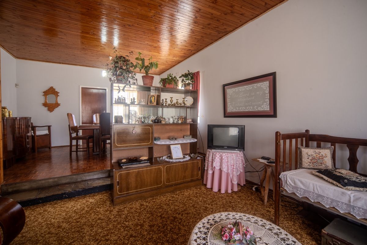 A living room featuring a timber-paneled ceiling, parquet flooring in the dining area, and a raised stone step transition.