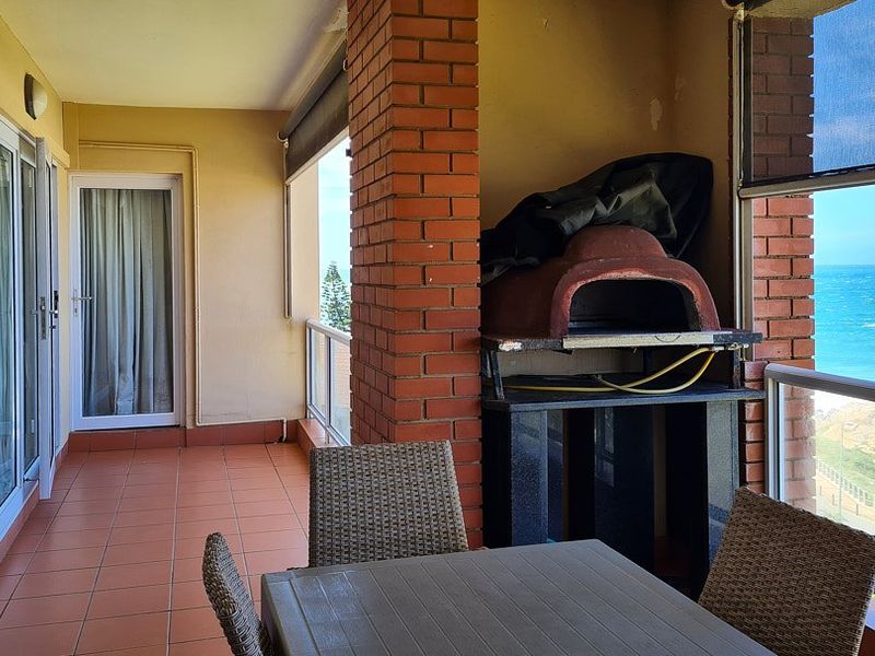 Covered balcony featuring a built-in pizza oven, tiled flooring, and glass balustrades with direct ocean views.
