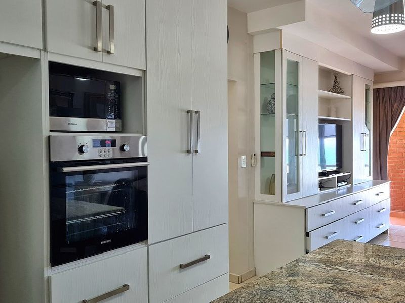Open plan living area featuring modern built-in cabinetry, integrated oven and microwave, granite countertops, and seamless transition to a balcony.