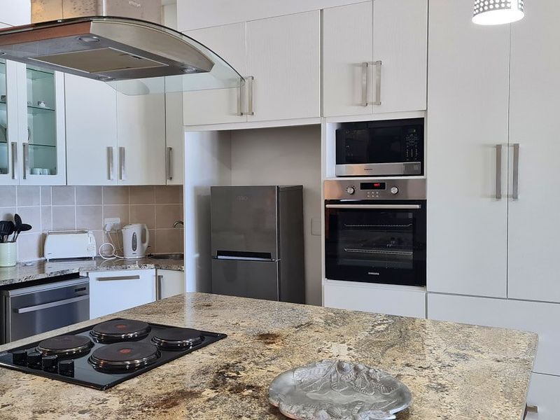 Modern kitchen featuring granite countertops, built-in oven, microwave, electric hob, extractor fan, and ample white cabinetry for storage.