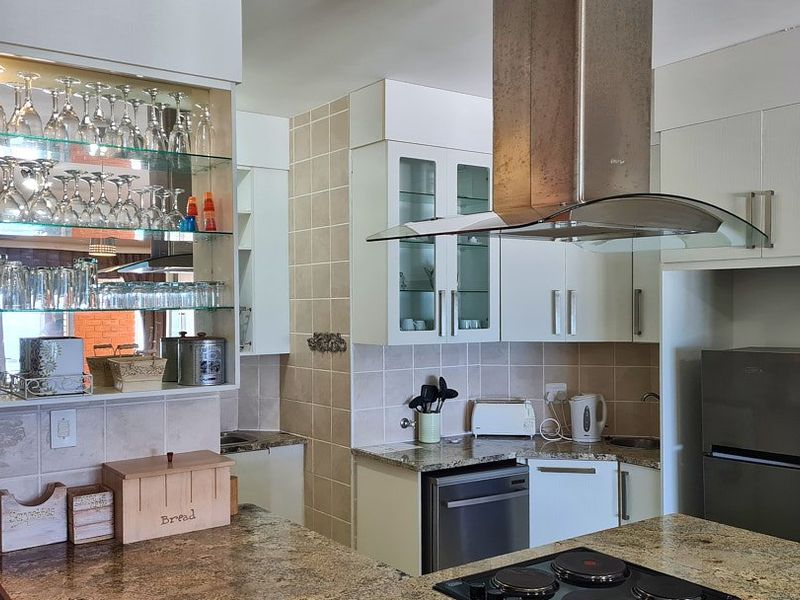 A functional kitchen featuring granite countertops, a stainless steel extractor fan, tiled backsplash, and ample built-in cabinetry with glass display shelving.