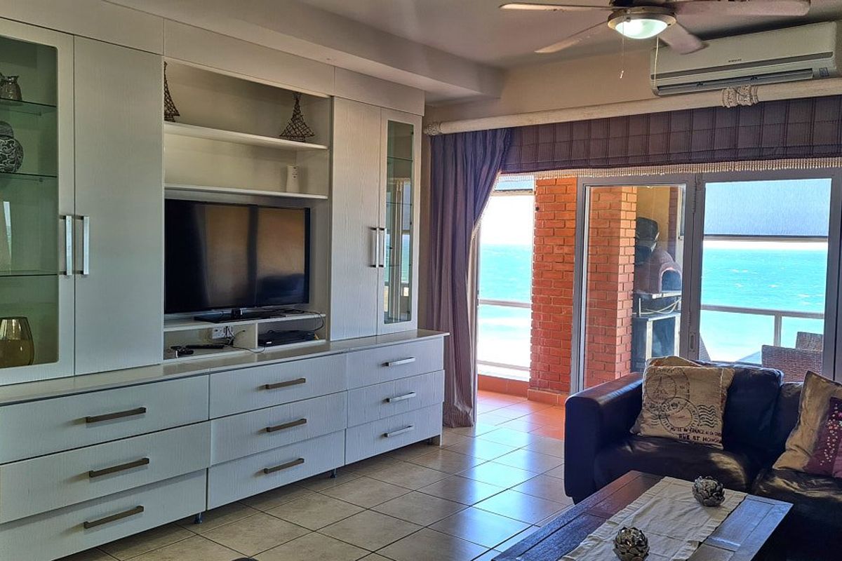 A bright living room featuring extensive built-in cabinetry, tiled flooring, and direct access to a balcony with ocean views.