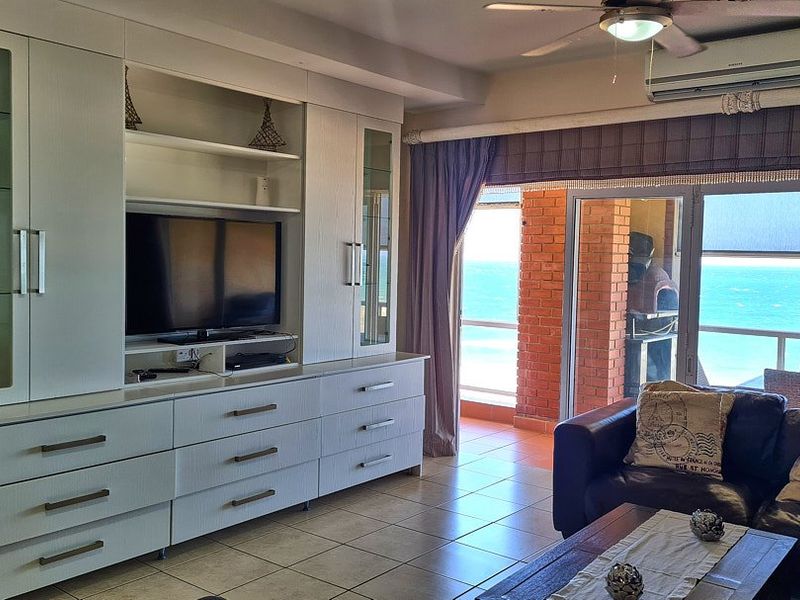 A bright living room featuring extensive built-in cabinetry, tiled flooring, and direct access to a balcony with ocean views.