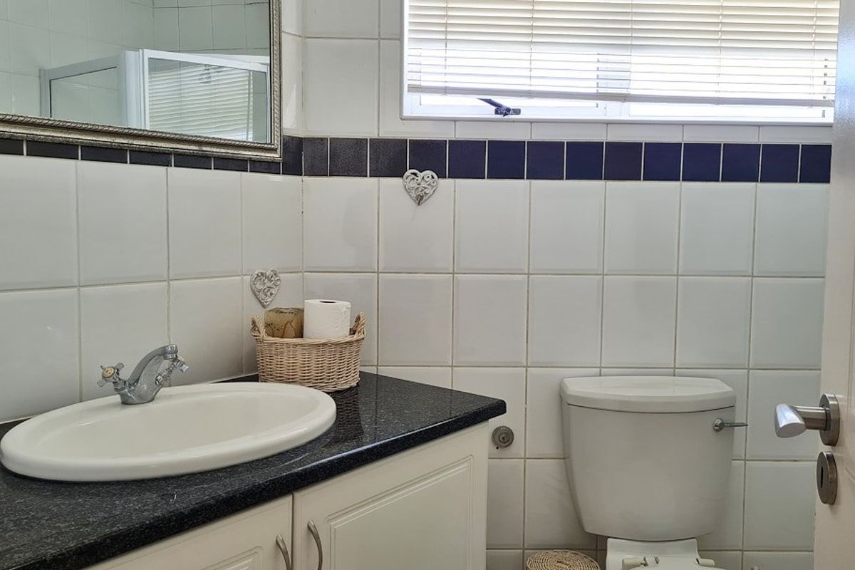 A functional bathroom featuring a vanity with granite countertop, drop-in basin, toilet, and tiled walls with a decorative border.