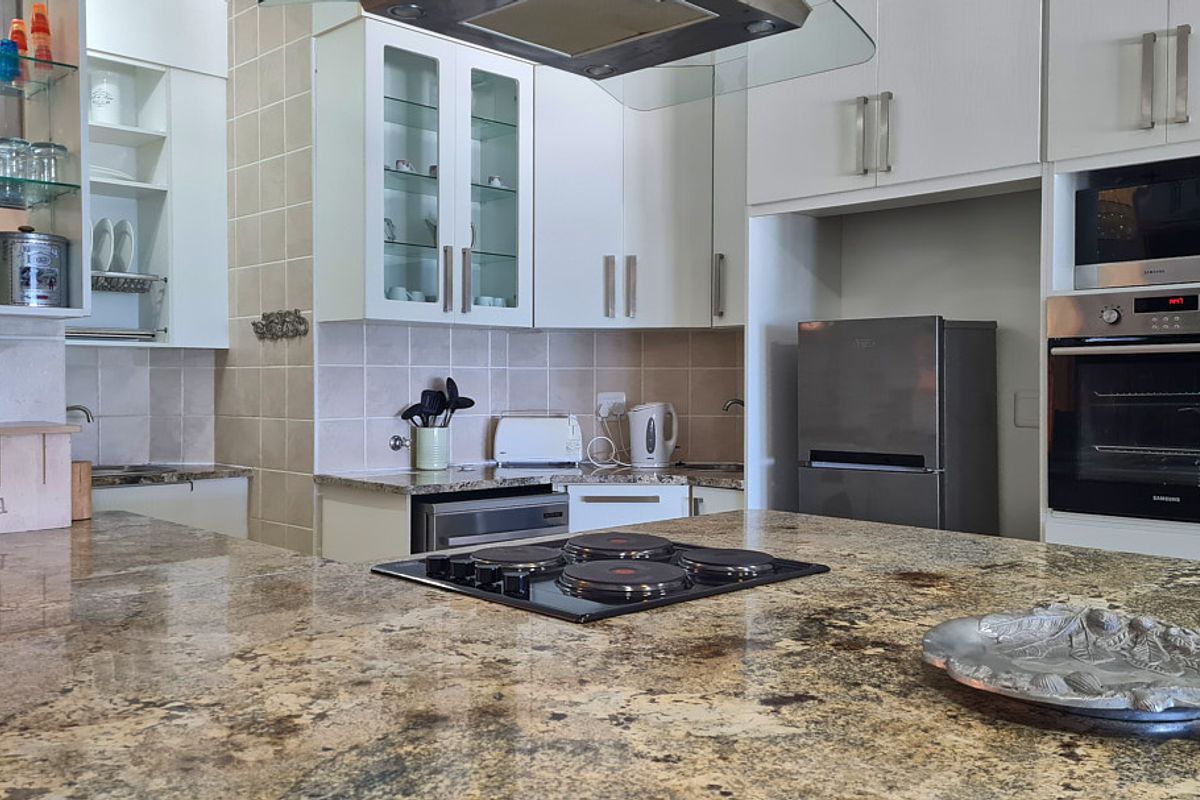 Modern kitchen featuring granite countertops, built-in oven, microwave, and electric hob with ample cabinetry and a tiled backsplash.