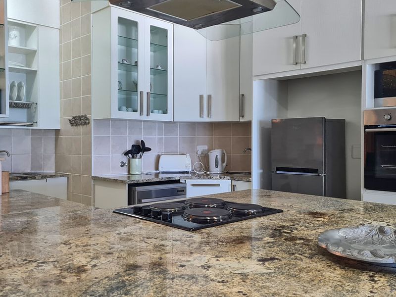 Modern kitchen featuring granite countertops, built-in oven, microwave, and electric hob with ample cabinetry and a tiled backsplash.