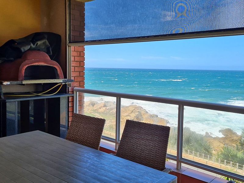 Covered balcony featuring a built-in braai, glass balustrade, and retractable blind, offering expansive ocean views.