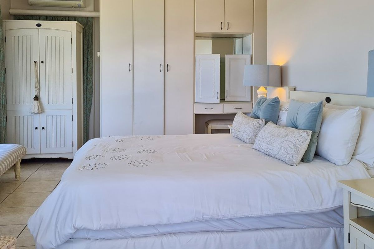 A well-maintained bedroom featuring built-in cupboards, a vanity area, tiled flooring, and an integrated air conditioning unit.