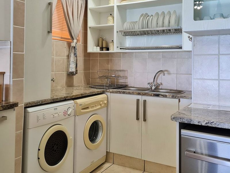 A functional laundry area featuring granite countertops, built-in cabinetry, a stainless steel sink, and tiled backsplash with space for under-counter appliances.