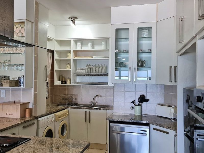 A functional kitchen featuring granite countertops, built-in oven, extractor fan, integrated dishwasher, and ample cabinetry with glass-fronted display units.