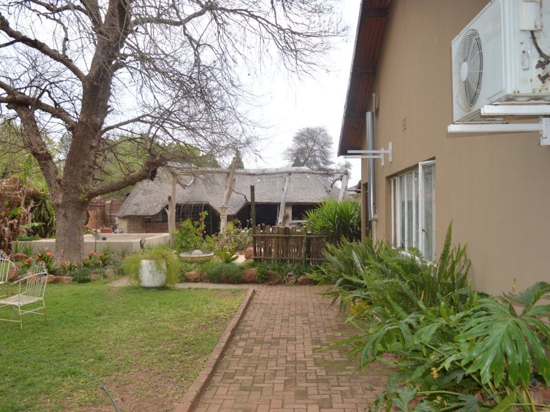 Rear garden area featuring a paved walkway, established trees, and a detached thatched roof structure.