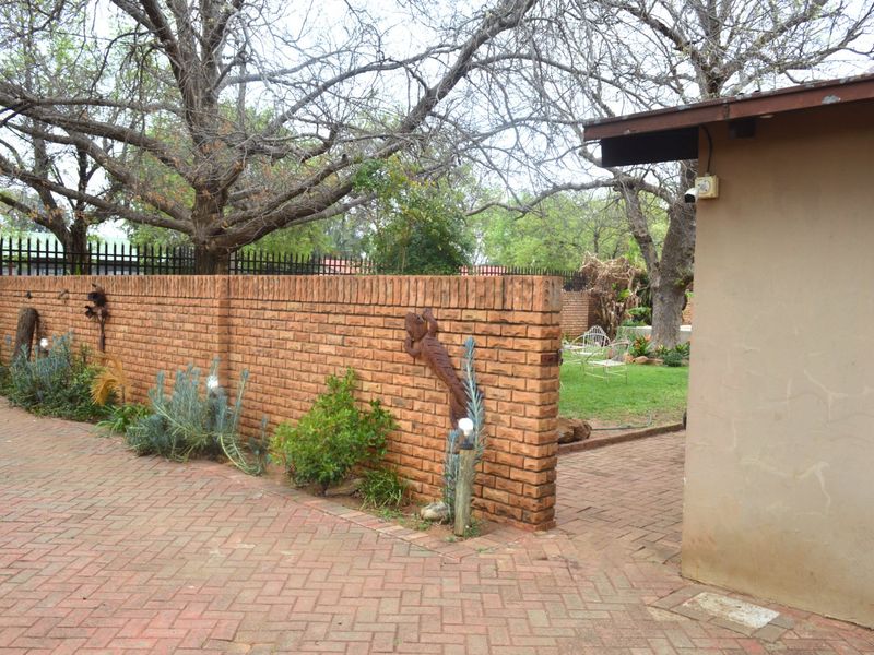 A rear exterior view featuring a brick boundary wall, paved driveway area, and mature trees in the garden setting.