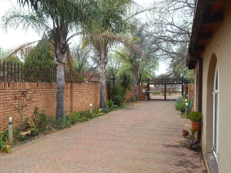 A private paved driveway leading to a secure metal gate, enclosed by a sturdy brick boundary wall with integrated security features.