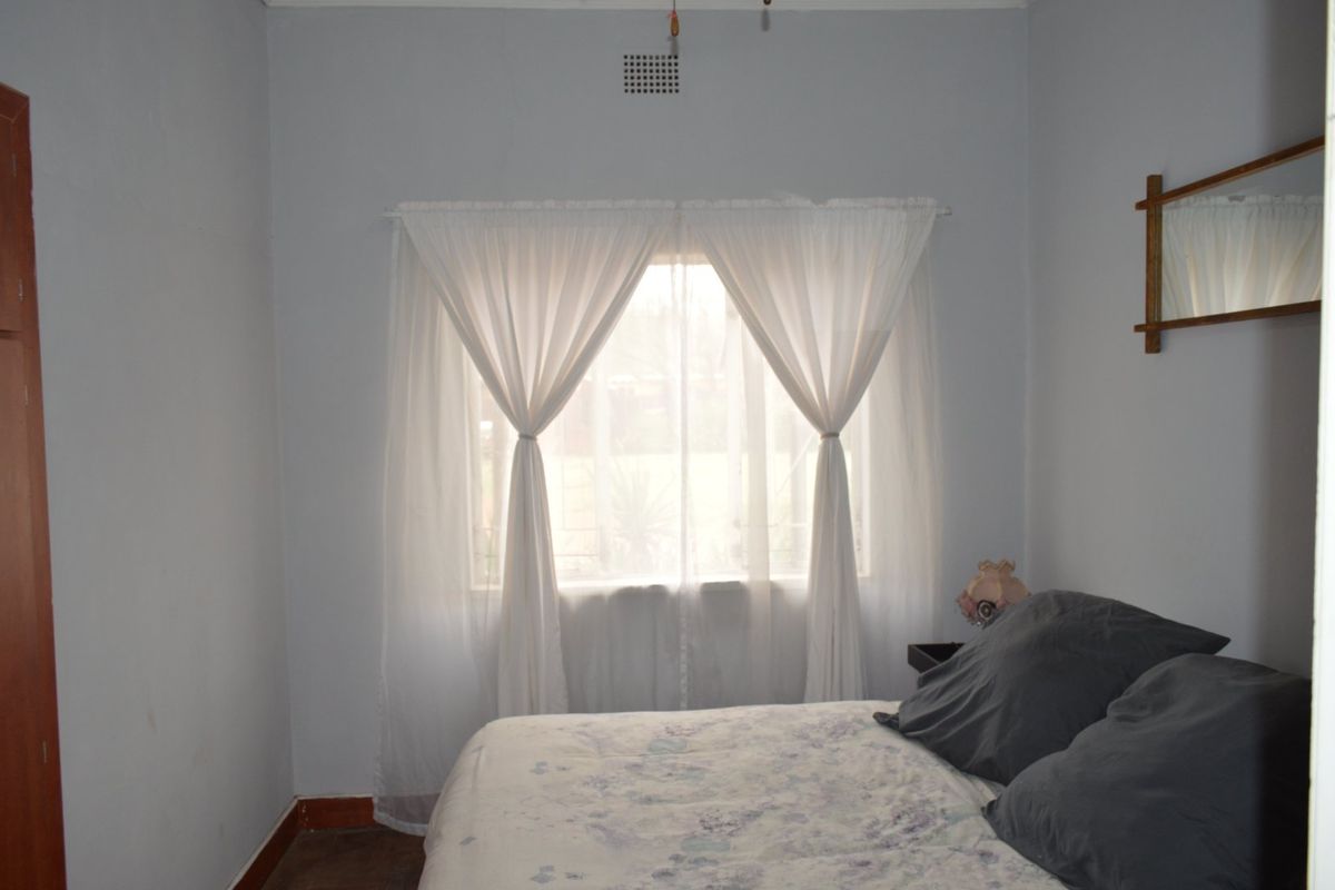 A simple bedroom featuring a built-in cupboard and a central window with natural light.