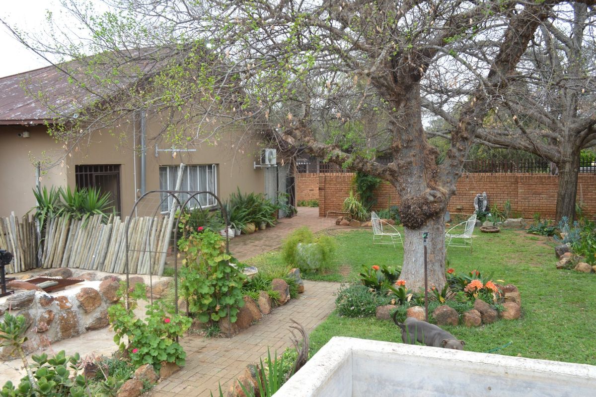 A rear garden view featuring a paved walkway, mature tree, and brick boundary wall, with access to the main house structure.