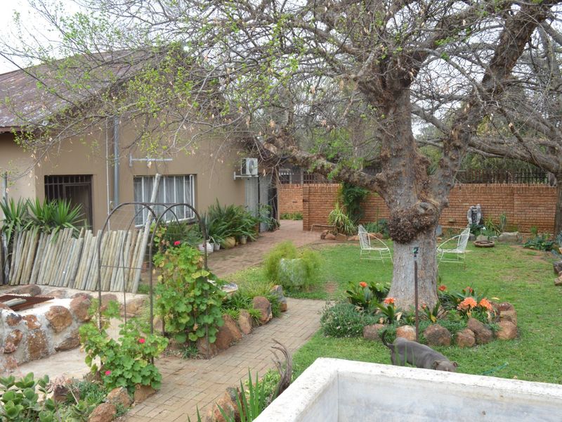 A rear garden view featuring a paved walkway, mature tree, and brick boundary wall, with access to the main house structure.