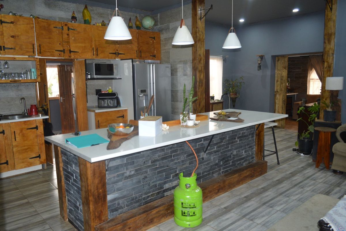 Rustic-style kitchen featuring a large island with stone veneer base, quartz countertop, wooden cabinetry, and modern pendant lighting.