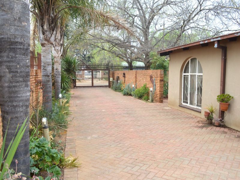 A paved driveway leading to a secure gated entrance, featuring a brick perimeter wall and an arched window on the side of the house.