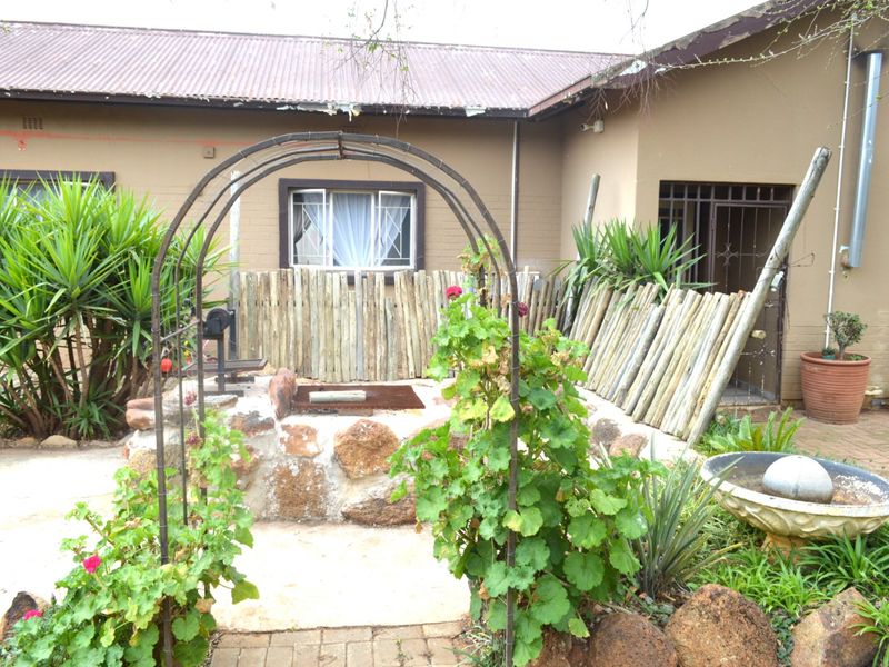 Rear exterior view featuring a garden area with a metal arch, stone retaining wall, timber fencing, and access to the main dwelling.