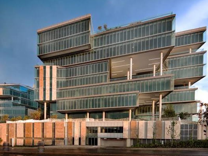 Modern commercial office building featuring a striking glass curtain wall facade, cantilevered levels, and stone-clad base with integrated parking access.