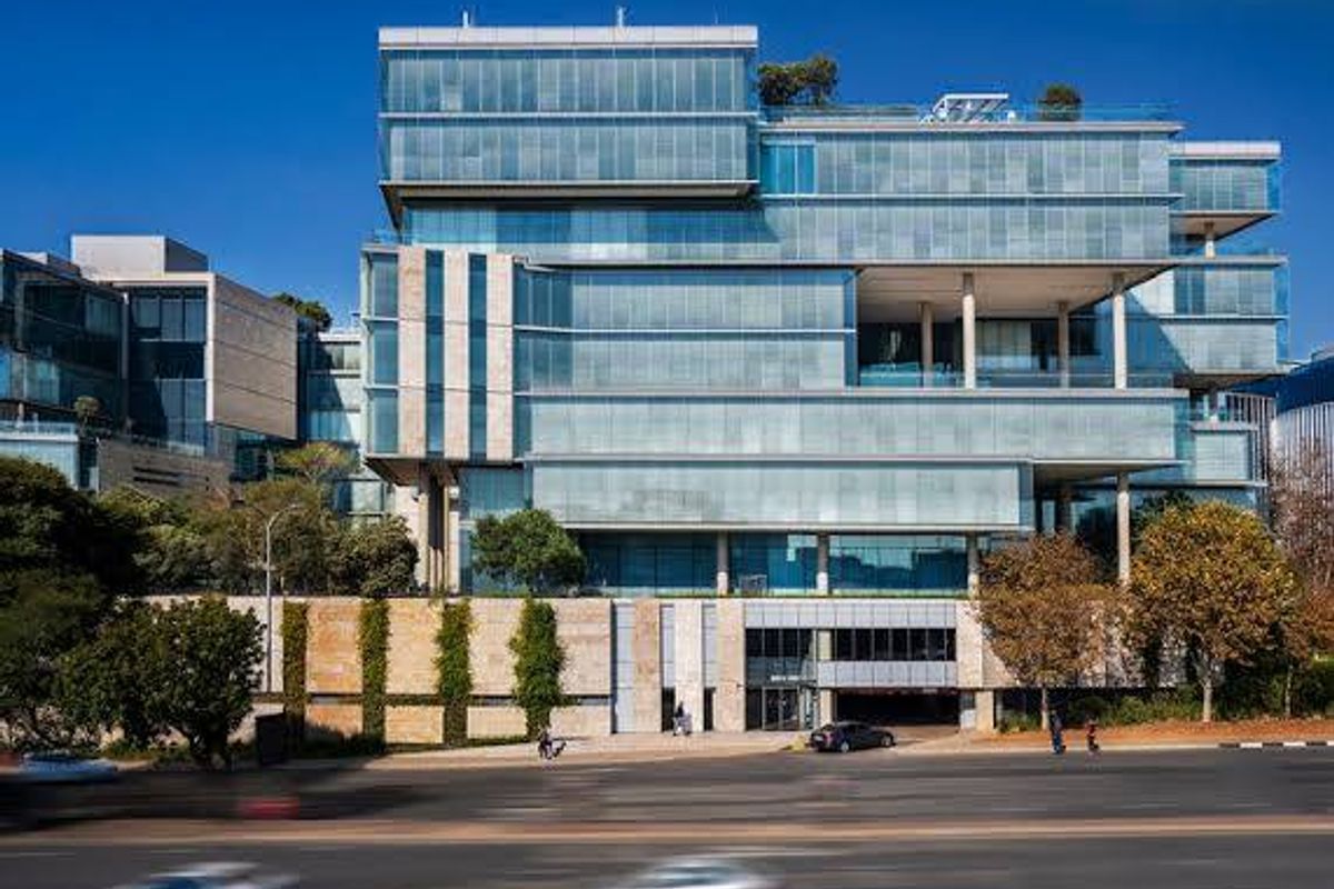 Modern commercial office building featuring a prominent glass curtain wall facade, stone cladding, and integrated covered parking entrance.