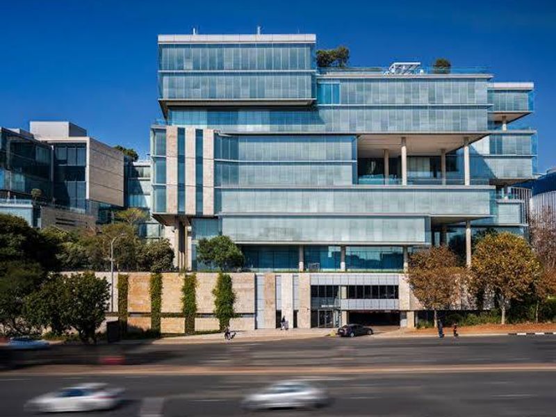 Modern commercial office building featuring a prominent glass curtain wall facade, stone cladding, and integrated covered parking entrance.