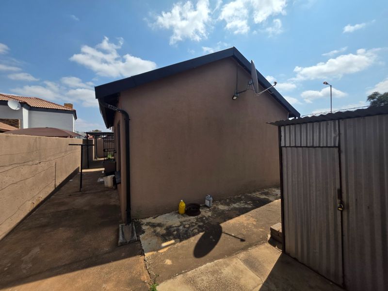 Rear exterior view of the property featuring a concrete paved yard, a corrugated metal storage shed, and boundary walling.
