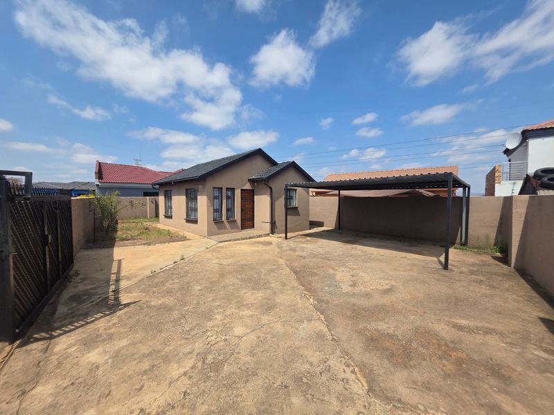 Front view of a detached house featuring a concrete driveway, a covered carport, and a perimeter wall with a security gate.