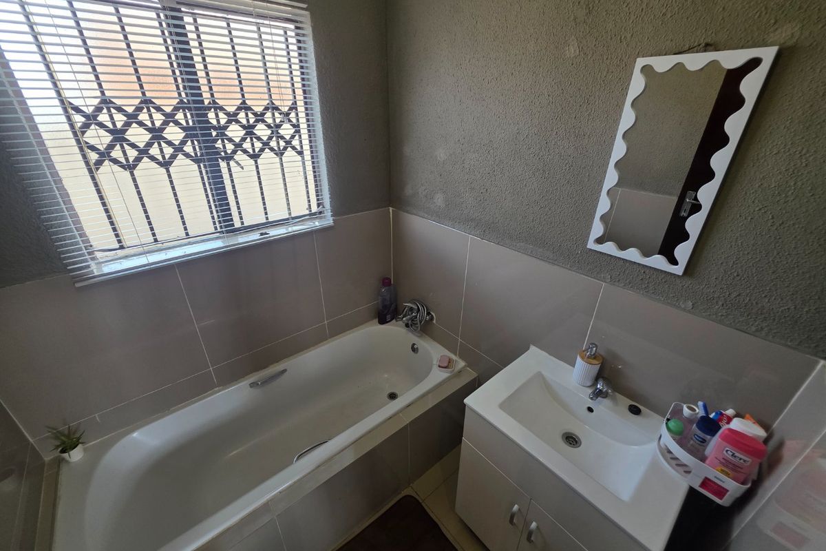 A functional bathroom featuring a bathtub, a modern vanity cabinet with basin, and a window fitted with security bars and blinds.