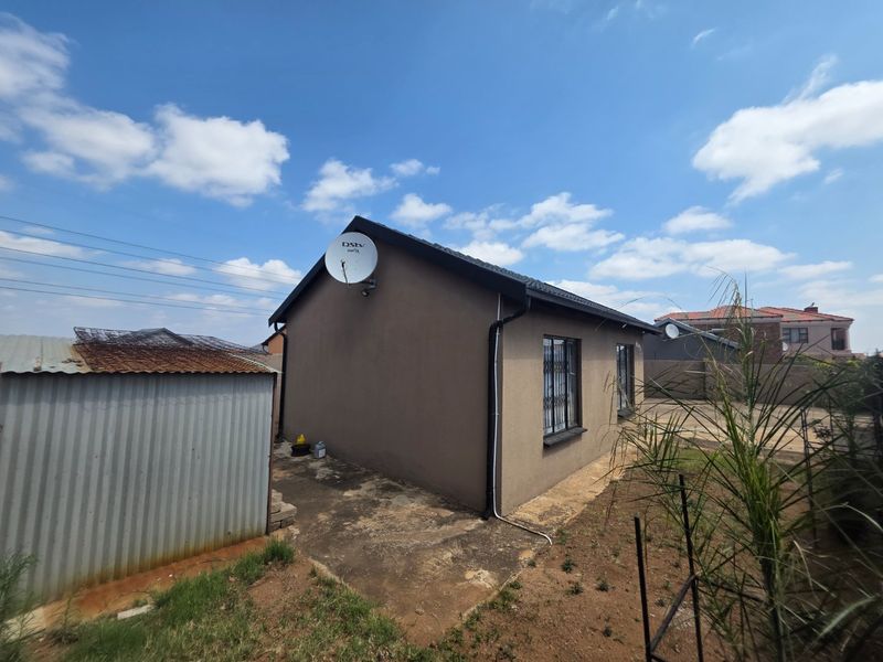 Rear view of the property featuring a concrete apron, security bars on windows, and a detached corrugated metal storage shed.