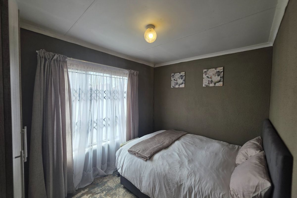 A cozy bedroom featuring a built-in wardrobe, security gate on the window, and neutral wall finishes.