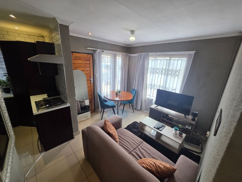 Open-plan living and kitchen area featuring tiled flooring, built-in cabinetry with a hob, and natural light through large windows with security gates.