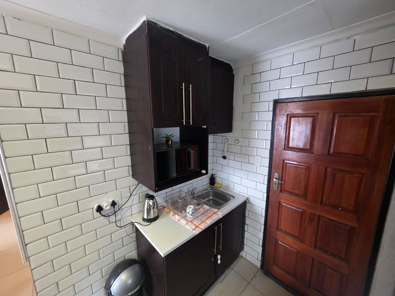 Compact scullery area featuring dark built-in cabinetry, a stainless steel sink, and white subway tile backsplash, providing functional prep and wash-up space.