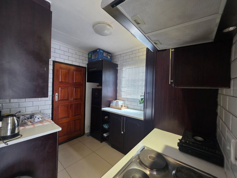 Compact kitchen featuring dark wood cabinetry, subway tile backsplash, and integrated cooking appliances with tiled flooring and direct exterior access.