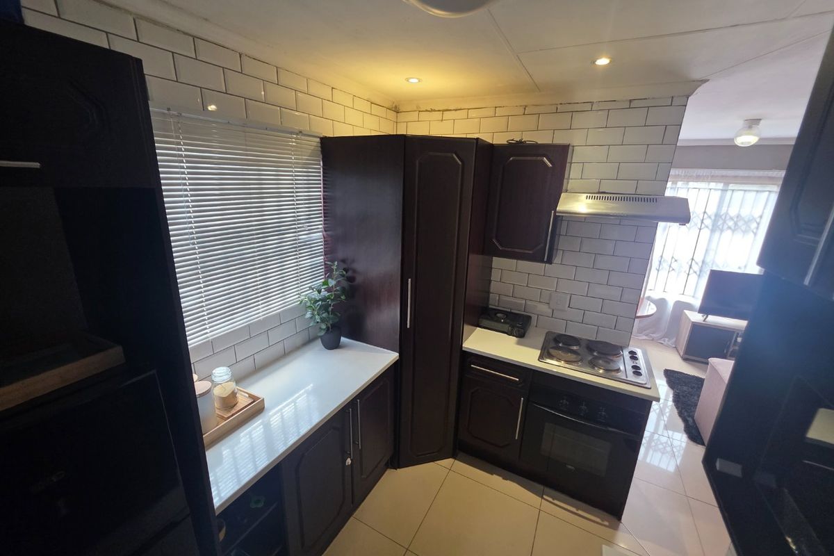 Compact kitchen featuring dark wood cabinetry, white subway tile backsplash, built-in oven, and electric hob, with an open-plan flow to the living area.